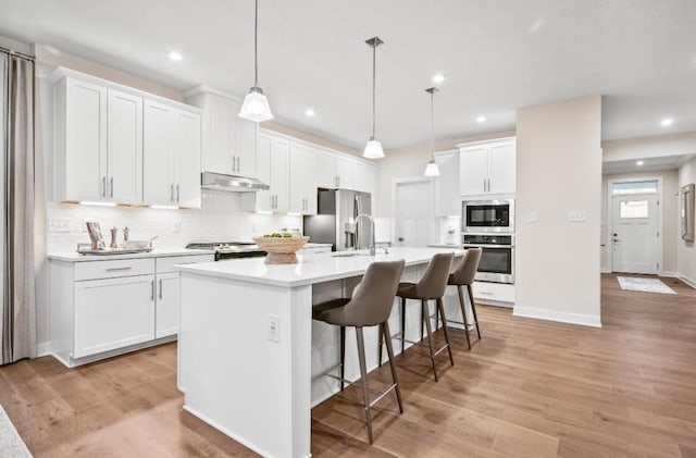 kitchen with a breakfast bar, appliances with stainless steel finishes, white cabinetry, hanging light fixtures, and an island with sink