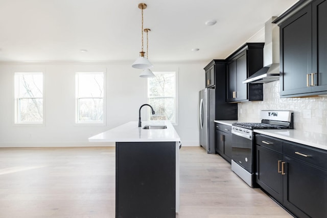 kitchen with wall chimney exhaust hood, sink, decorative light fixtures, a center island with sink, and stainless steel appliances