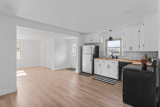 kitchen featuring sink, butcher block countertops, hanging light fixtures, stainless steel fridge, and dishwasher