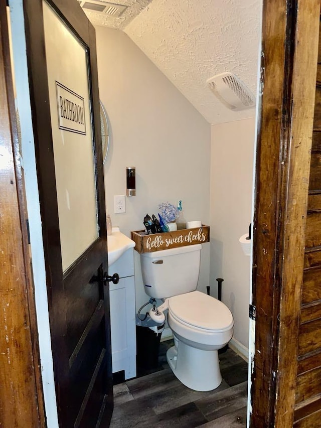 bathroom with vanity, wood-type flooring, a textured ceiling, vaulted ceiling, and toilet