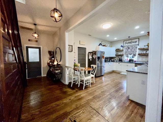 kitchen with stainless steel refrigerator with ice dispenser, pendant lighting, dark hardwood / wood-style flooring, and white cabinets