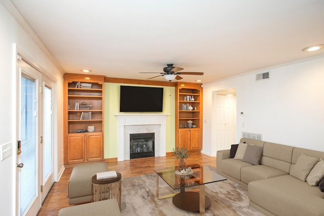 living room featuring a tiled fireplace, hardwood / wood-style floors, crown molding, and built in shelves