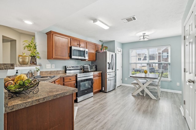 kitchen with appliances with stainless steel finishes, sink, and light hardwood / wood-style flooring