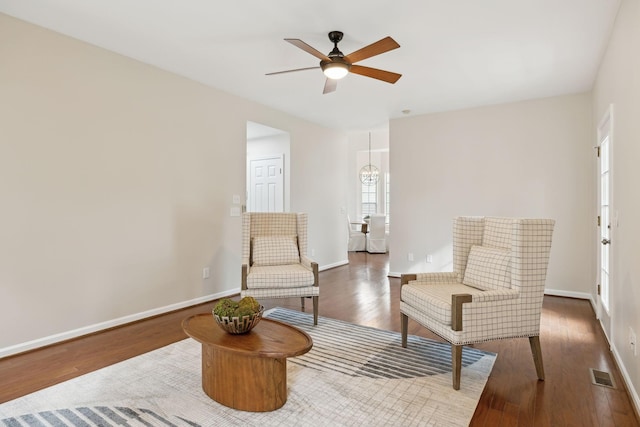 sitting room featuring dark wood-type flooring and ceiling fan with notable chandelier