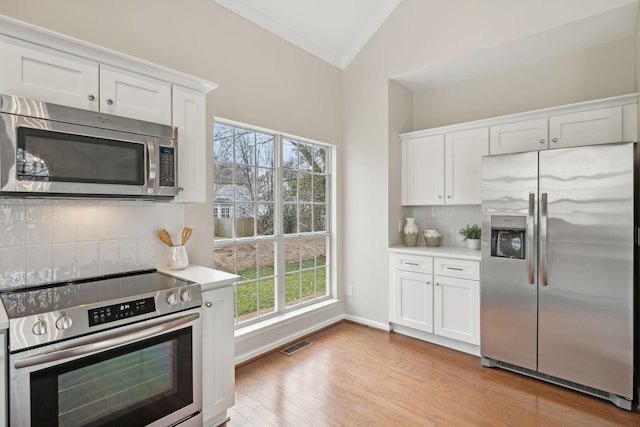 kitchen featuring lofted ceiling, light wood-type flooring, appliances with stainless steel finishes, decorative backsplash, and white cabinets