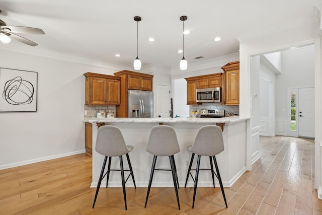 kitchen with stainless steel appliances, hanging light fixtures, a breakfast bar area, and light hardwood / wood-style flooring