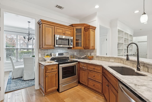 kitchen featuring sink, appliances with stainless steel finishes, hanging light fixtures, light hardwood / wood-style floors, and light stone countertops