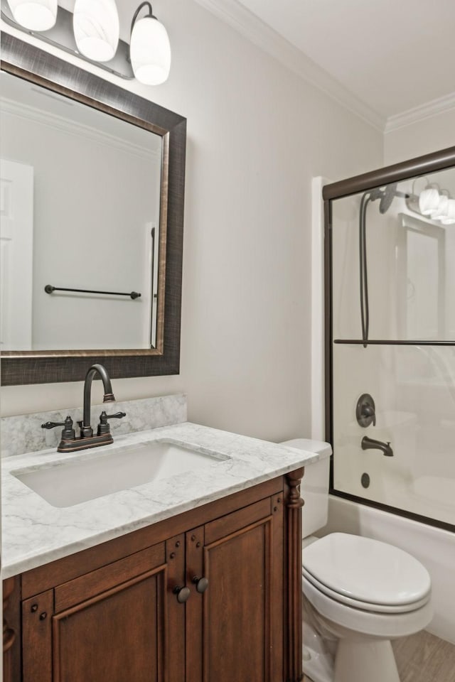 full bathroom featuring ornamental molding, combined bath / shower with glass door, vanity, and toilet