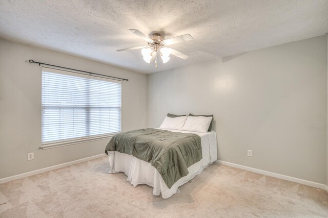 bedroom with ceiling fan, light colored carpet, and a textured ceiling