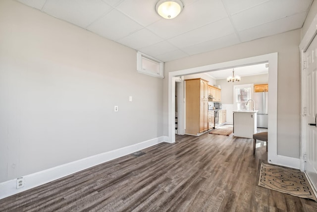 spare room with a drop ceiling, a notable chandelier, and dark wood-type flooring