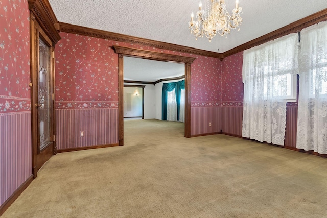 carpeted spare room with ornamental molding, a notable chandelier, and a textured ceiling