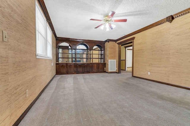 unfurnished room featuring ceiling fan, ornamental molding, a textured ceiling, and carpet flooring