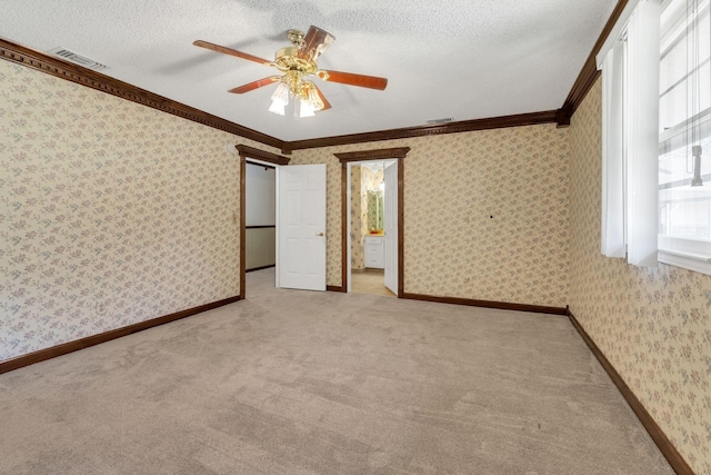 unfurnished bedroom with ensuite bath, ceiling fan, carpet floors, ornamental molding, and a textured ceiling