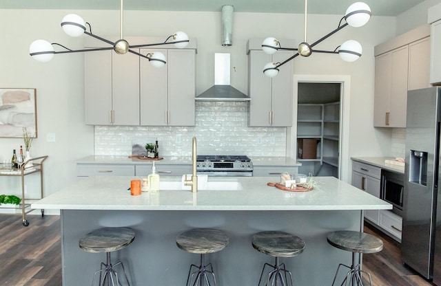 kitchen featuring gray cabinetry, wall chimney range hood, stainless steel appliances, and a kitchen bar