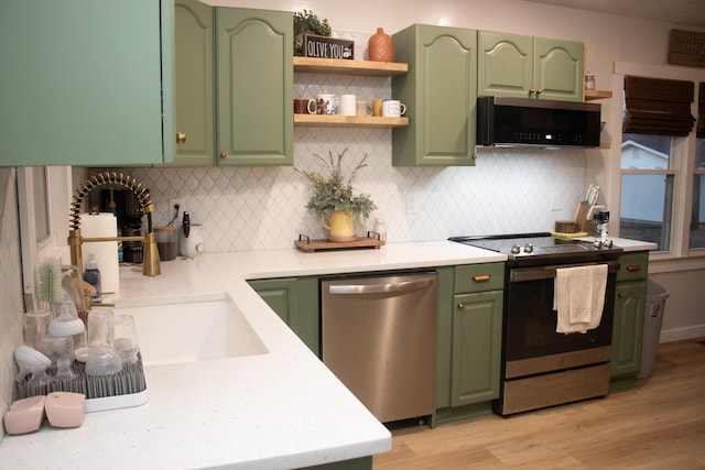 kitchen with tasteful backsplash, stainless steel appliances, green cabinets, and light hardwood / wood-style flooring