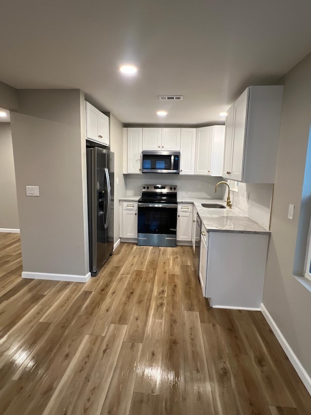 kitchen with light wood finished floors, baseboards, appliances with stainless steel finishes, white cabinetry, and a sink