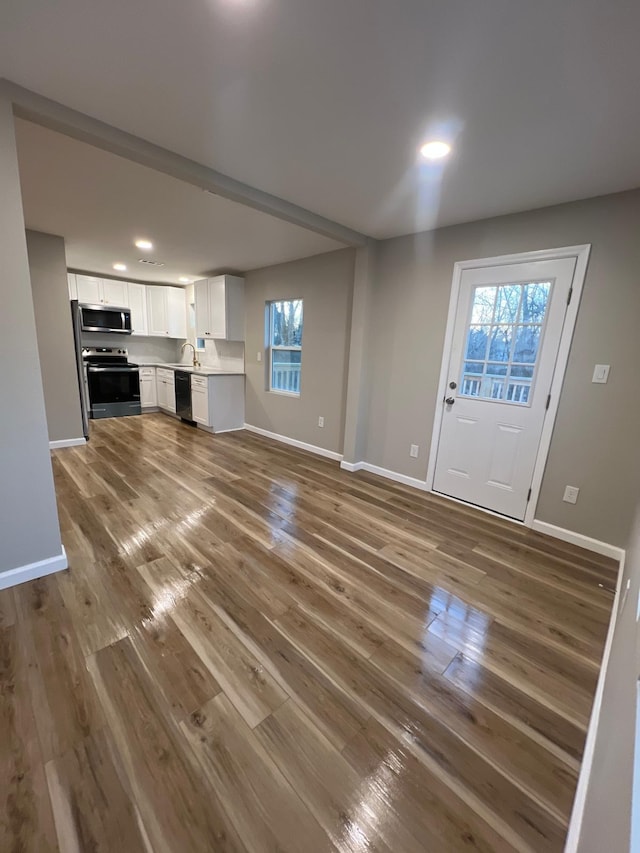 unfurnished living room featuring a sink, baseboards, and wood finished floors