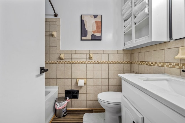 bathroom featuring tile walls, a tub to relax in, vanity, and toilet