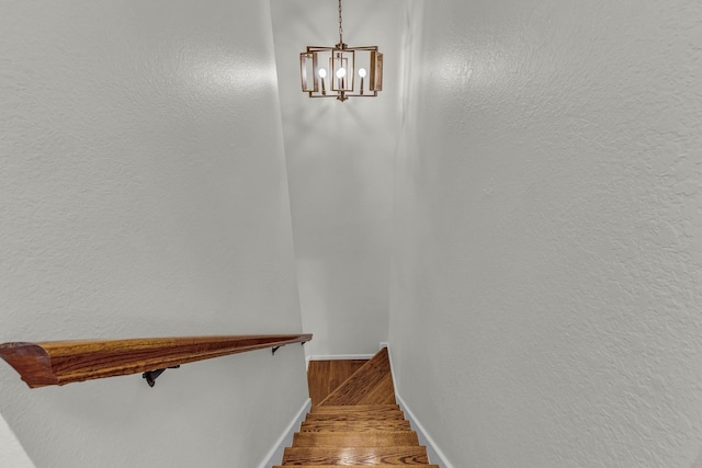 stairs featuring a notable chandelier, baseboards, and wood finished floors