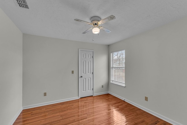 empty room featuring visible vents, light wood-style floors, a ceiling fan, a textured ceiling, and baseboards