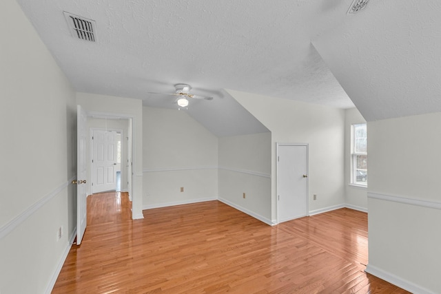 additional living space featuring light wood finished floors, baseboards, visible vents, vaulted ceiling, and a textured ceiling