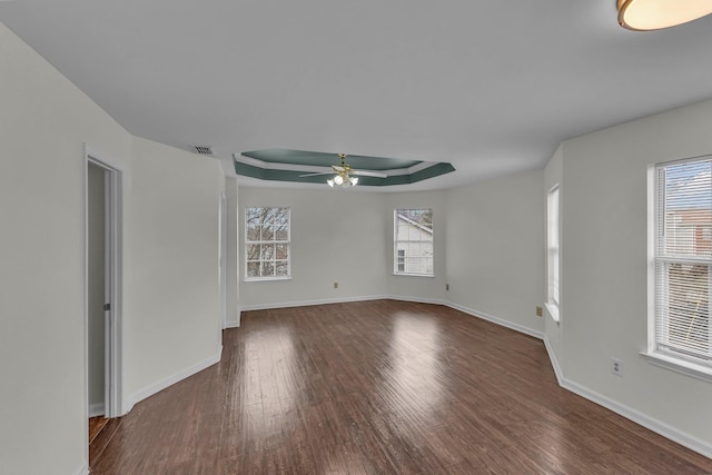 spare room with a wealth of natural light, a tray ceiling, dark wood finished floors, and ceiling fan