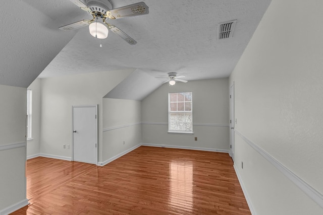 bonus room featuring a textured ceiling, wood finished floors, visible vents, and a ceiling fan