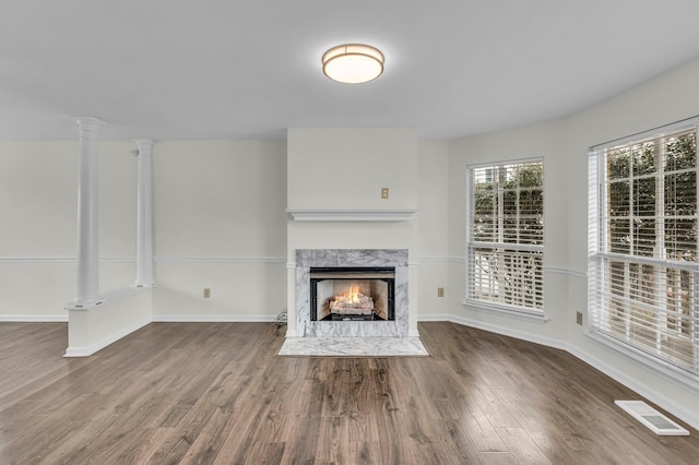 unfurnished living room with baseboards, visible vents, wood finished floors, ornate columns, and a high end fireplace