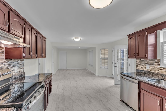 kitchen with decorative backsplash, appliances with stainless steel finishes, a sink, under cabinet range hood, and baseboards