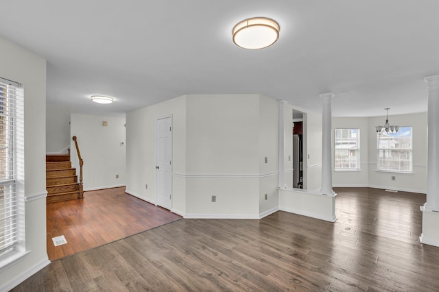 unfurnished room with dark wood-style flooring, ornate columns, an inviting chandelier, baseboards, and stairs