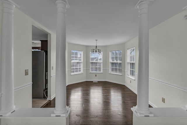 unfurnished dining area with ornate columns, baseboards, dark wood finished floors, and a notable chandelier