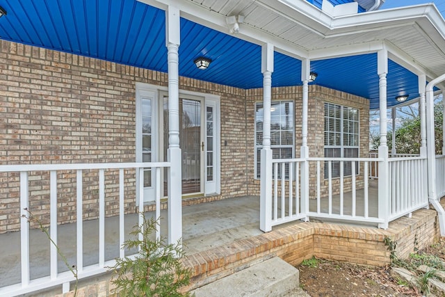 view of exterior entry with a porch and brick siding