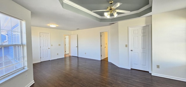 unfurnished bedroom with baseboards, ceiling fan, dark wood-type flooring, a tray ceiling, and crown molding