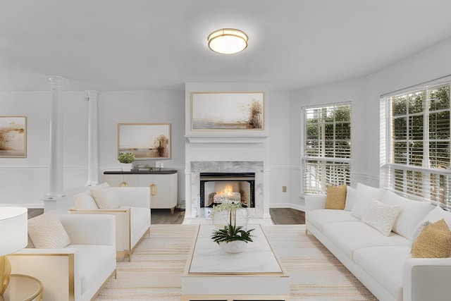 living area with light wood finished floors, a premium fireplace, and ornate columns