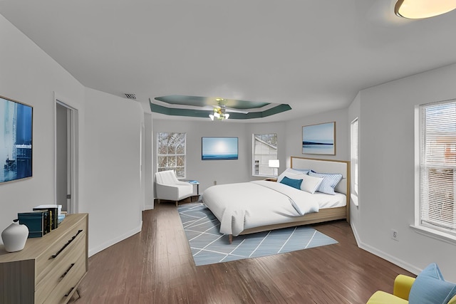 bedroom with ceiling fan, multiple windows, a raised ceiling, and dark wood-style flooring