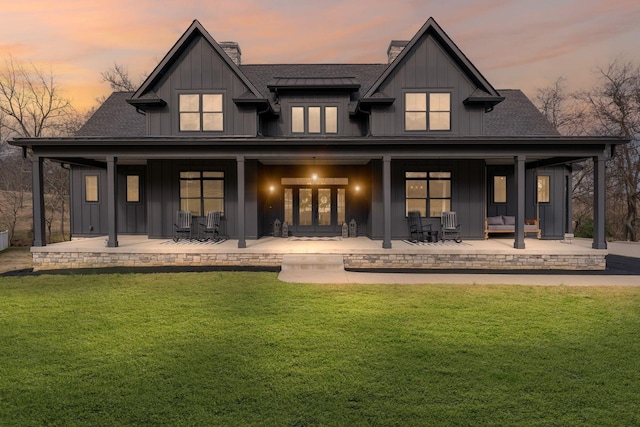 back house at dusk featuring a patio area and a lawn