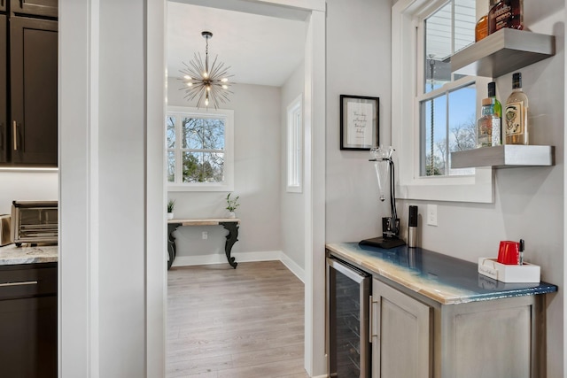 bar with wine cooler, a notable chandelier, dark brown cabinets, and light hardwood / wood-style floors