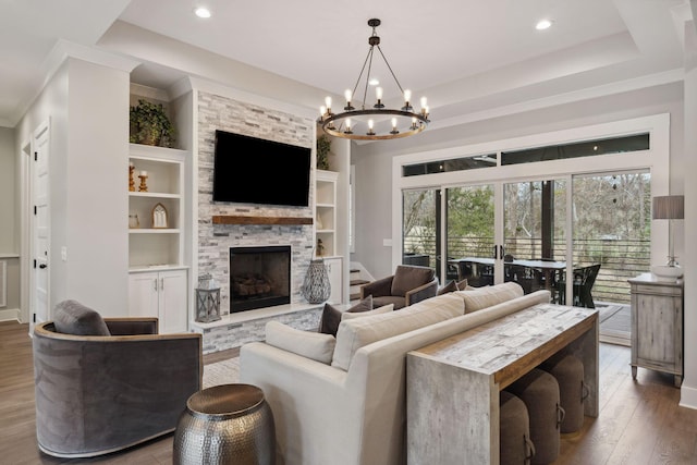 living room with a stone fireplace, hardwood / wood-style flooring, ornamental molding, a tray ceiling, and built in shelves