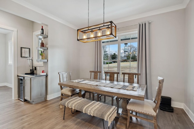 dining area featuring wine cooler, indoor bar, ornamental molding, and light wood-type flooring