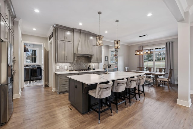 kitchen featuring appliances with stainless steel finishes, a breakfast bar, pendant lighting, a large island with sink, and custom exhaust hood