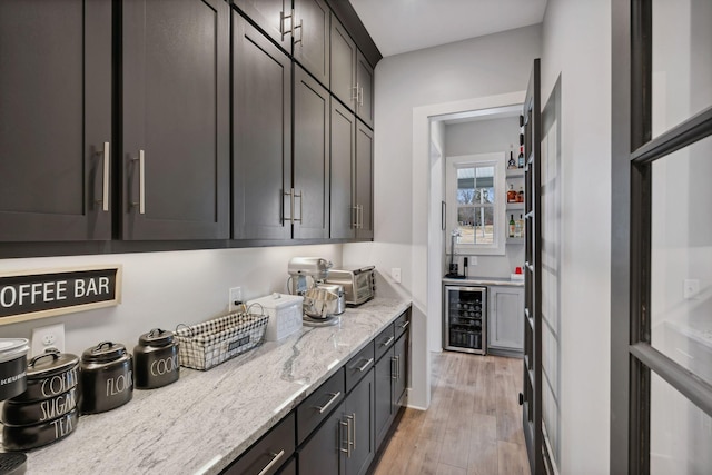 kitchen featuring wine cooler, dark brown cabinetry, light hardwood / wood-style floors, and light stone counters