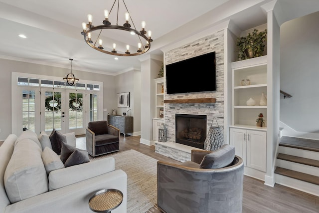 living room with a stone fireplace, wood-type flooring, ornamental molding, built in shelves, and french doors