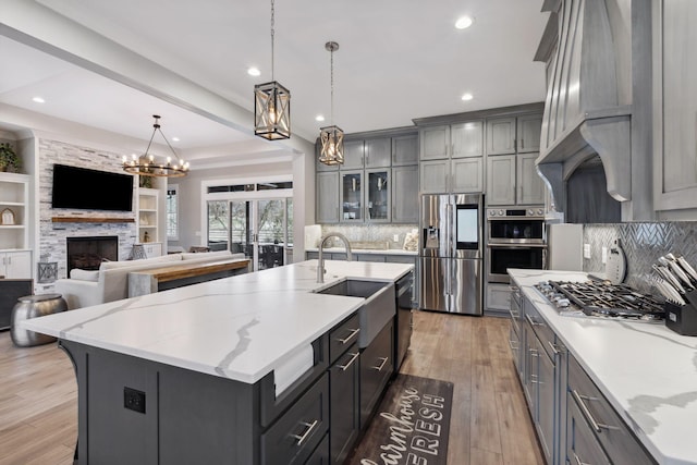 kitchen with gray cabinets, a stone fireplace, hanging light fixtures, stainless steel appliances, and a spacious island