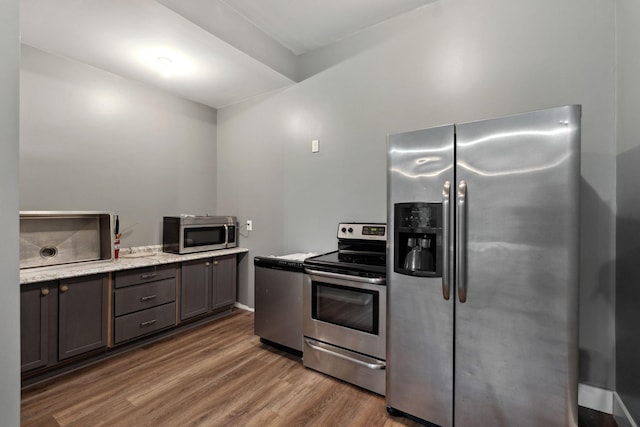 kitchen featuring light stone counters, dark brown cabinetry, appliances with stainless steel finishes, and dark hardwood / wood-style flooring