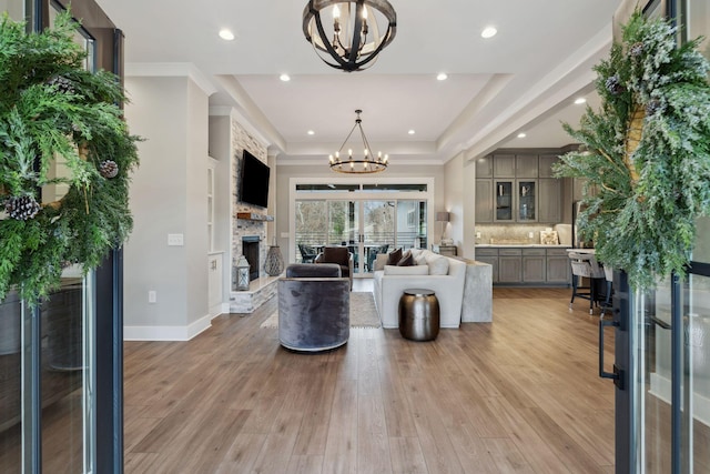 living room featuring a tray ceiling, a notable chandelier, a fireplace, and light hardwood / wood-style floors