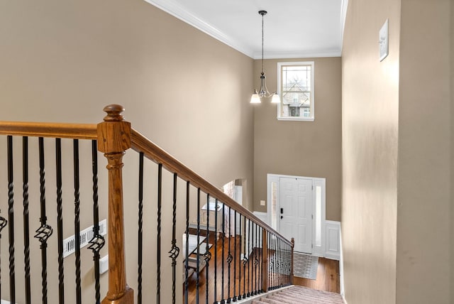 staircase with a towering ceiling, ornamental molding, hardwood / wood-style floors, and a notable chandelier