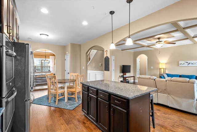 kitchen featuring pendant lighting, stainless steel appliances, dark brown cabinetry, a kitchen island, and dark stone counters