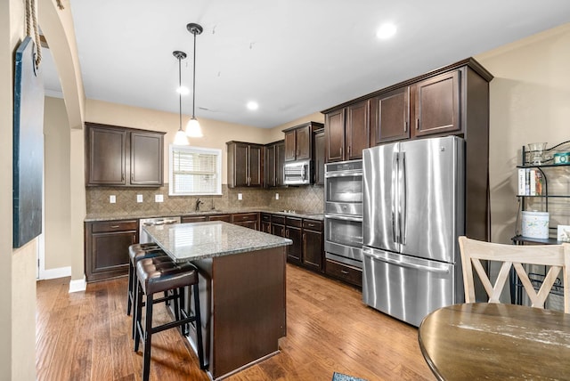 kitchen featuring sink, stainless steel appliances, a center island, a kitchen breakfast bar, and decorative light fixtures