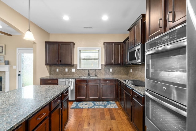 kitchen with sink, light stone counters, hanging light fixtures, appliances with stainless steel finishes, and hardwood / wood-style floors