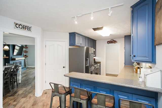 kitchen with blue cabinetry, appliances with stainless steel finishes, kitchen peninsula, and light hardwood / wood-style flooring